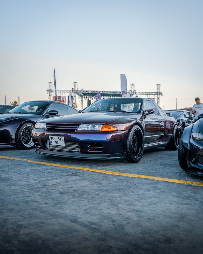 Car exhibition in İzmir showcasing iconic Japanese models like the Nissan GT-R under a clear evening sky.